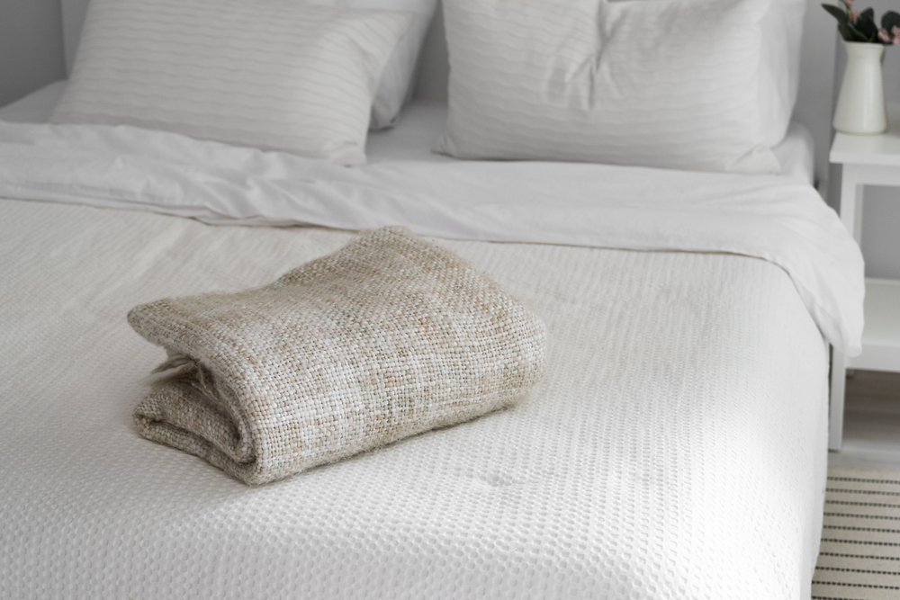Dormitorio con ropa de cama blanca y una manta tejida beige, que aportan frescura y confort. La combinación de textiles suaves y naturales crea un espacio ideal para un descanso reparador y sereno.